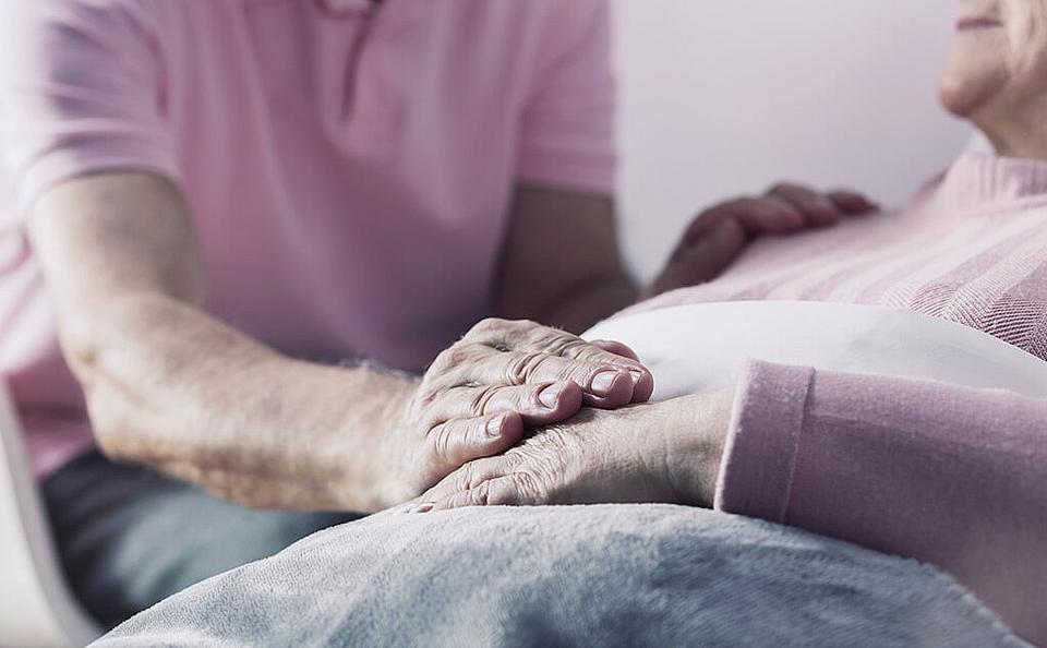 Hand einer im Bett liegenden Person wird gehalten